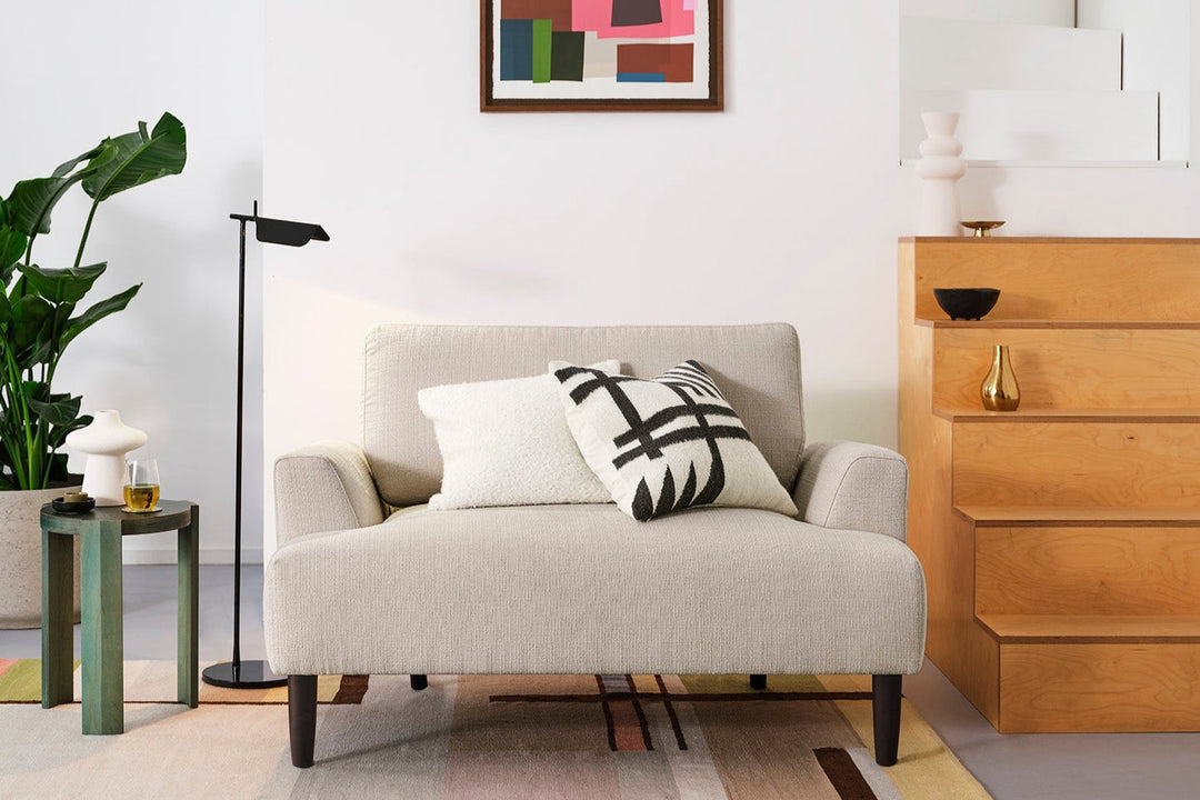 Beige sofa with decorative pillows in a living room setting with a wooden cabinet and plant.