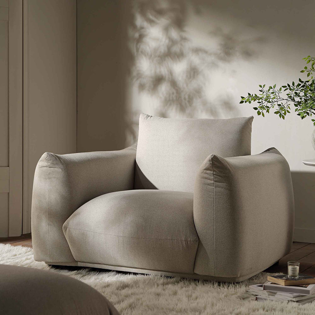 Beige armchair in a modern living room setting with a plant and coffee table.