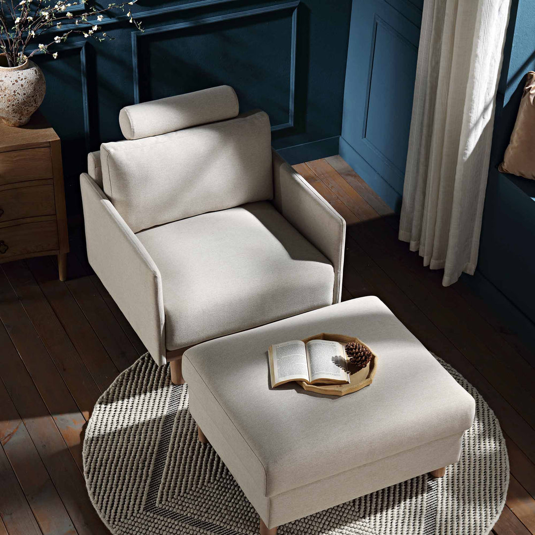 Beige armchair and ottoman with a book on a small table in a room with blue walls and wooden floor.