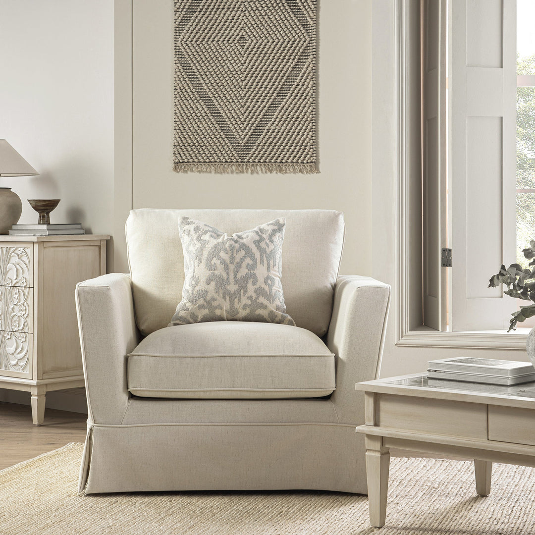 Beige armchair with a patterned pillow in a living room setting.