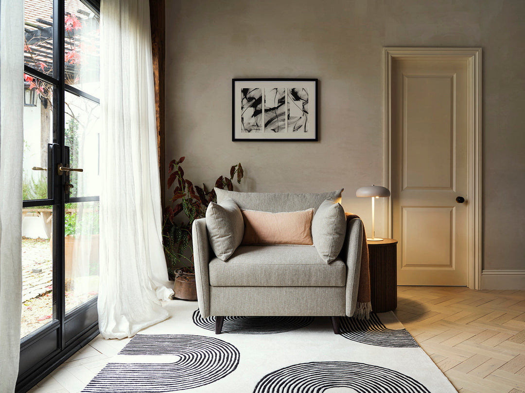Living room with a gray armchair, decorative pillows, and a patterned rug.