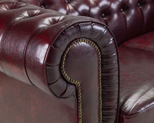 Close-up of a brown leather sofa with tufted backrest and decorative nailhead trim.