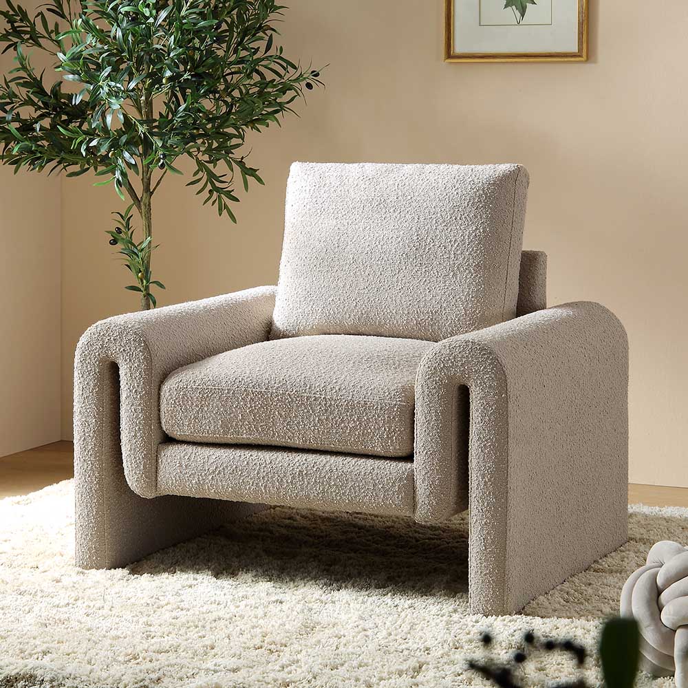 Beige armchair in a living room setting with a plant and framed picture on the wall.