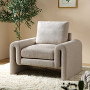Beige armchair in a living room setting with a plant and framed picture on the wall.