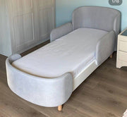 Gray upholstered bed in a room with wooden flooring and a wardrobe.