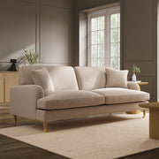 Beige sofa in a modern living room with large windows and neutral decor.