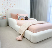 White bed with pink bedding and decorative pillows in a room with floral wallpaper and curtains.