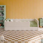 Load image into Gallery viewer, A children's bed with a cream upholstered frame and green bedding, styled in a room with a yellow wavy wall, a mint green bookshelf, and a checkered floor.