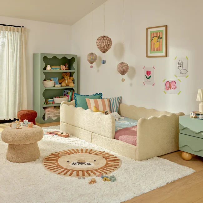 Children's bedroom with a beige sofa, colorful pillows, and a green bookshelf.