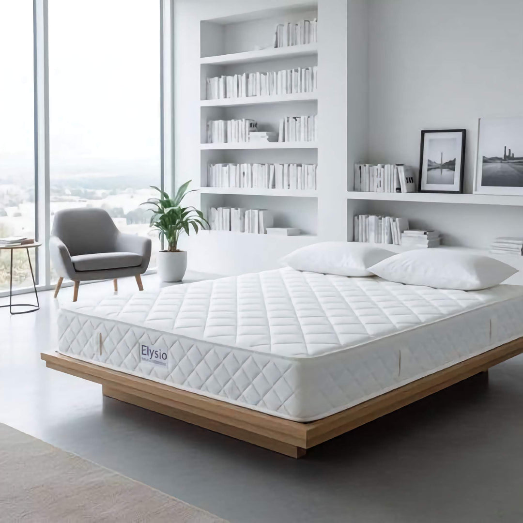 White mattress on a wooden bed frame in a modern bedroom with bookshelves and decor.