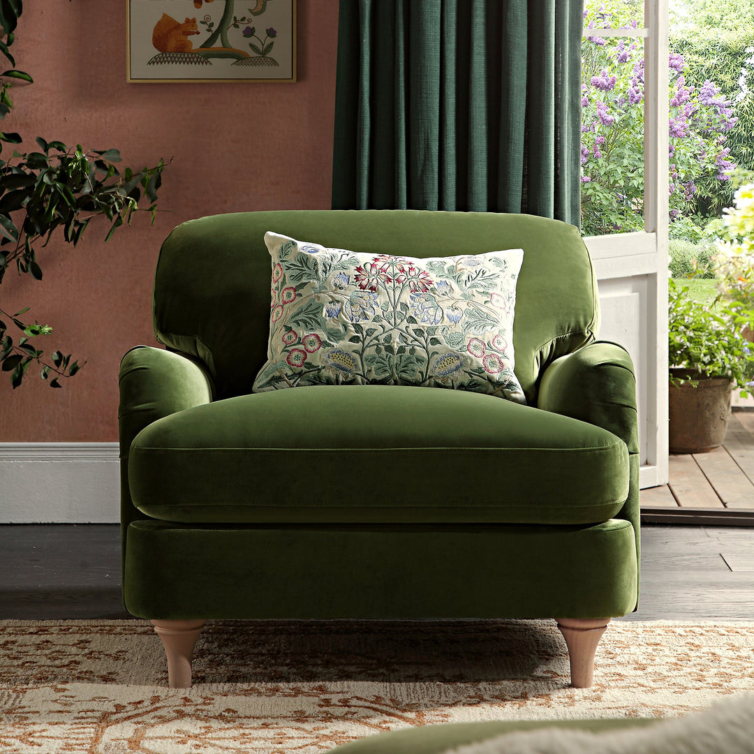 Green armchair with a floral pillow in a room with pink walls and a window.