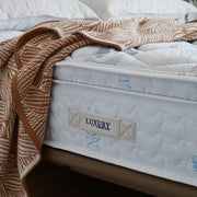 Mattress with a blanket draped over it, featuring a 'Luxury' label.