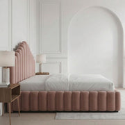 Pink velvet bed in a stylish bedroom with white walls and wooden flooring.