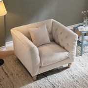 Beige armchair in a living room setting with a lamp and small table in the background.