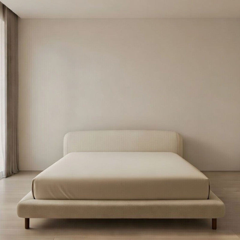Beige bed in a minimalistic room with beige walls and wooden floor.