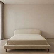 Beige bed in a minimalistic room with beige walls and wooden floor.