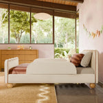 Load image into Gallery viewer, A mid-century modern upholstered bed with a cream bouclé headboard and footboard, styled in a bedroom with a pink wall, wood dresser, and large windows showing a green outdoor view.