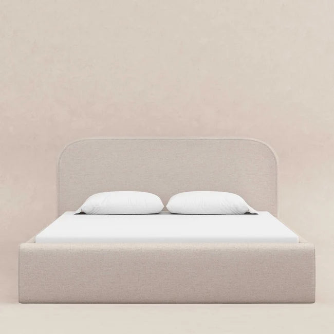 Beige bed with white bedding against a light pink wall