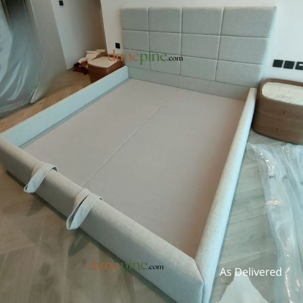 Bed with a gray headboard and mattress in a room setting, showing 'As Delivered' text.