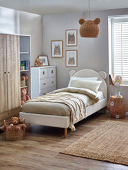 Children's bedroom with a bed, teddy bears, and framed pictures on a light gray wall.