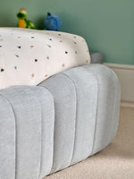 Load image into Gallery viewer, Gray ottoman with a colorful cushion on a carpeted floor against a green wall.