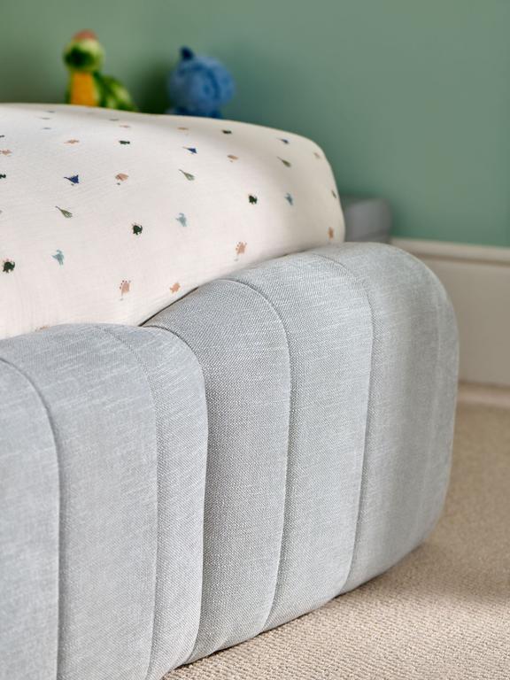 Gray ottoman with a colorful cushion on a carpeted floor against a green wall.