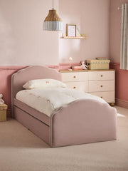 Pink bed in a child's bedroom with a dresser and decorative items.